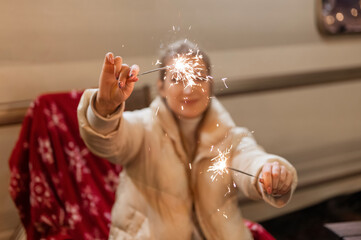 sparklers bengal fire sticks in female hands holding young candid woman sitting on a chair with a red plaid outdoor on happy new year and merry christmas winter holidays eve night. sparkling sparks
