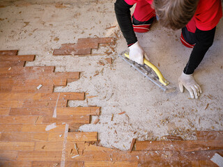Craftsman in workwear who, using the rabot, removes excess glue left on the floor after removing...