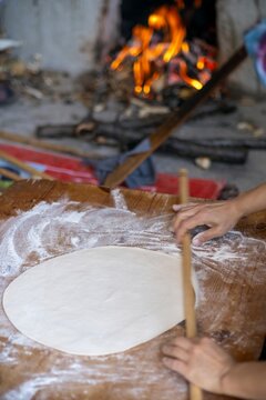 Female Hands Of Baker Rolls Dough In Flour On Wooden Board On Table With A Rolling Pin, In Bakery Shop, Woman Making Pizza Using Traditional Recipe At Home.