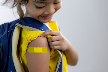  Asian young girl showing her arm with yellow bandage after got vaccinated or inoculation, child...