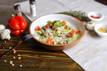 Salad with lettuce, cherry tomatoes, radish slices, herbs are served on a dark tabletop on a linen napkin. Hot red pepper and whole white champignon, rosemary branch.