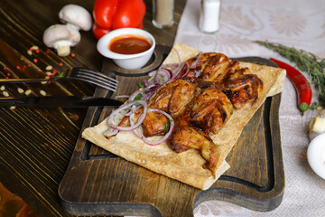 On a dark countertop, a light linen napkin, on a cutting board Fried four quails in pita bread with red onion rings, on a linen napkin, cutlery, red pepper, rosemary branch.