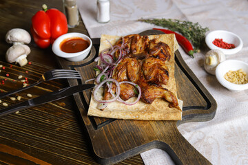 On a dark countertop, a light linen napkin, on a cutting board Fried four quails in pita bread with red onion rings, on a linen napkin, cutlery, red pepper, rosemary branch.