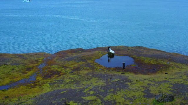 Aerial panoramic view of two newlyweds and camera man on edge of shore 