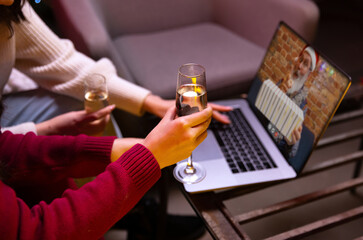 Female hands with champange glasses. Girls sitting at home and celebrate holiday, New yera with family by video call