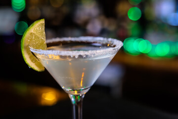 In a funnel-shaped glass with a long stem, the alcoholic cocktail is opaque, opaque, with a slice of lime on the sugared edge of the glass. Filming of the bar menu against the background