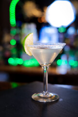 In a funnel-shaped glass with a long stem, the alcoholic cocktail is opaque, opaque, with a slice of lime on the sugared edge of the glass. Filming of the bar menu against the background
