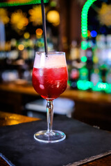 In a tall glass, an opaque, blood-red cocktail with high white foam on top and a black straw. 