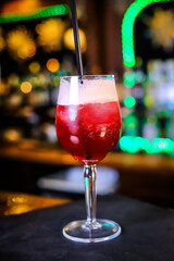 In a tall glass, an opaque, blood-red cocktail with high white foam on top and a black straw. 