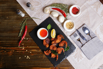 Shrimp is served with sauce. Tempura king prawns, sliced lemon, green basil leaves are served on a black stone stand. Cutlery, hot pepper pods, spices in bowls, white mushrooms.