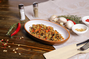 On a dark countertop Pilaf .In an oval dish, pilaf with black rice is served, on a linseed sallet, cutlery, a pair of salt and pepper, spices