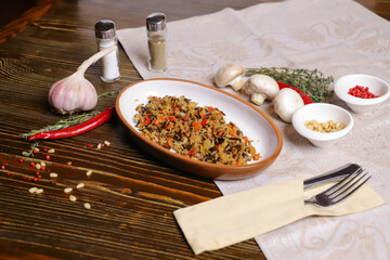 On a dark countertop Pilaf .In an oval dish, pilaf with black rice is served, on a linseed sallet, cutlery, a pair of salt and pepper, spices