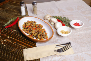 On a dark countertop Pilaf .In an oval dish, pilaf with black rice is served, on a linseed sallet, cutlery, a pair of salt and pepper, spices