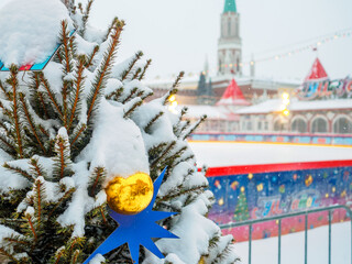 Shiny yellow Christmas ball on a snow-covered Christmas tree and blurred background of the Moscow Kremlin. Decorations for the celebration of the new year at the fair on Red Square in Moscow.