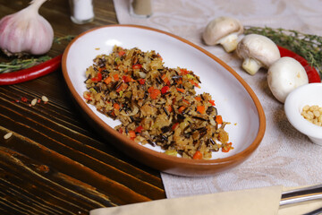 On a dark countertop Pilaf .In an oval dish, pilaf with black rice is served, on a linseed sallet, cutlery, a pair of salt and pepper, spices