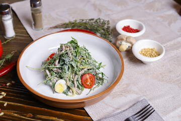 On a dark countertop, a light linen napkin, on a cutting board Served salad with rucola leaves, boiled tongue cut into long slices with sauce A couple of salt and pepper, cutlery, red peppers decorate