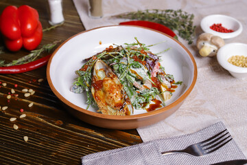 On a dark countertop, a light linen napkin, on a cutting board  Salad with mussels, rucola, red caviar, shrimps in a round dish, cutlery, pepper-salt steam, whole red pepper, hot pepper pod