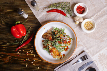 On a dark countertop, a light linen napkin, on a cutting board  Salad with mussels, rucola, red caviar, shrimps in a round dish, cutlery, pepper-salt steam, whole red pepper, hot pepper pod