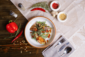 On a dark countertop, a light linen napkin, on a cutting board  Salad with mussels, rucola, red caviar, shrimps in a round dish, cutlery, pepper-salt steam, whole red pepper, hot pepper pod