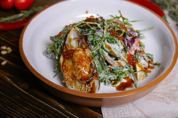 On a dark countertop, a light linen napkin, on a cutting board  Salad with mussels, rucola, red caviar, shrimps in a round dish, cutlery, pepper-salt steam, whole red pepper, hot pepper pod