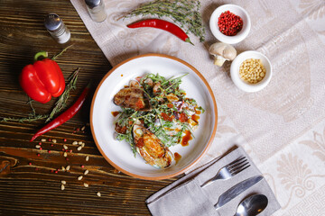 On a dark countertop, a light linen napkin, on a cutting board  Salad with mussels, rucola, red caviar, shrimps in a round dish, cutlery, pepper-salt steam, whole red pepper, hot pepper pod