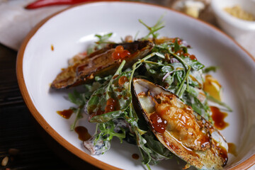 On a dark countertop, a light linen napkin, on a cutting board  Salad with mussels, rucola, red caviar, shrimps in a round dish, cutlery, pepper-salt steam, whole red pepper, hot pepper pod