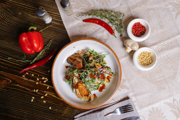 On a dark countertop, a light linen napkin, on a cutting board  Salad with mussels, rucola, red caviar, shrimps in a round dish, cutlery, pepper-salt steam, whole red pepper, hot pepper pod