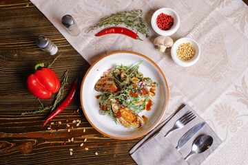 On a dark countertop, a light linen napkin, on a cutting board  Salad with mussels, rucola, red caviar, shrimps in a round dish, cutlery, pepper-salt steam, whole red pepper, hot pepper pod
