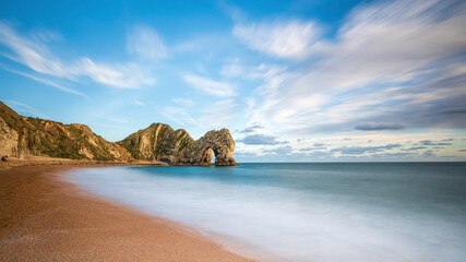 Fototapeta na wymiar Durdle Door, in Dorset, on the South coast of England. The natural rock arch is a famous landmark. Slow shutter speed to smooth out the water and the clouds