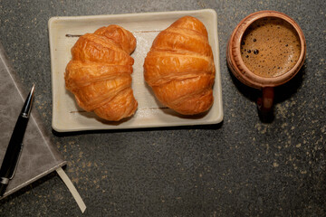 Breakfast food croissant in plate and coffee on stone table.