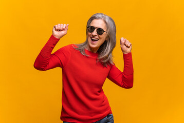 Horizontal portrait of hilarious senior woman in sunglasses dancing isolated on yellow. Middle-aged...