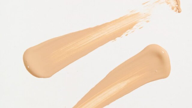 Macro shot and slow motion of a brush, applicator, smear, concealer isolated on white background. Advertising professional cosmetics. Closeup of a cosmetic liquid foundation or cream beige color. 4k