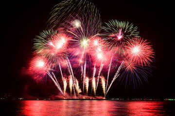 Amazing beautiful colorful fireworks display on celebration night, showing on the sea beach with multi color of reflection on water	
