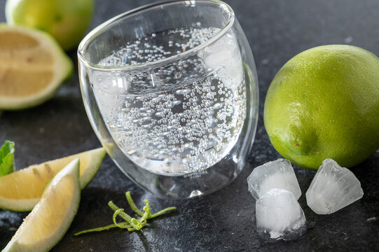 Wasserglas daneben liegen Eisw&uuml;rfel, Zitronenviertel eine ganze Limette und Zesten