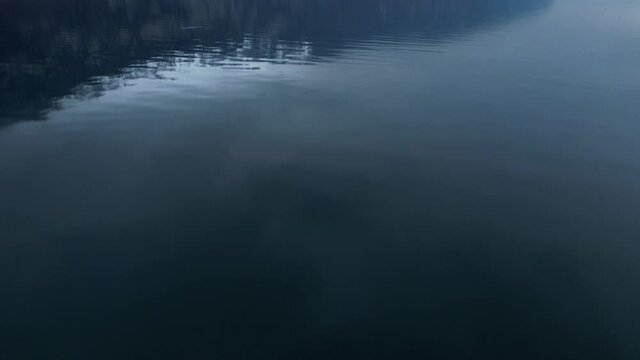 Slow tilt up shot over calm water and snowy rocky cliffs of a lake, aerial