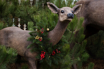 Russia, Park Loga, 13.12.2021. Sculpture of a Christmas deer fawn with a fir wreath around its neck in the park in winter  - obrazy, fototapety, plakaty