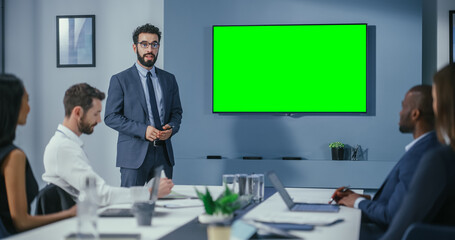 Office Conference Room Meeting Presentation: Handsome Businessman Talks, Uses Green Screen Chroma Key Wall TV. Successfully Presenting e-Commerce Product to Group of Multi-Ethnic Investors