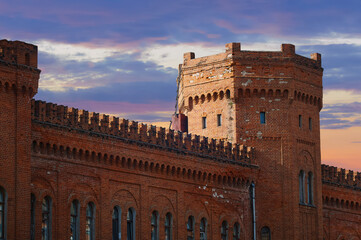 Fototapeta premium The tower of the fortress is made of red brick. Old town building in medieval style. Breaking down the walls. Redecorating. Dramatic sky with clouds at sunset. Blagoveshchensk, Russia.