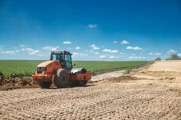 Earthwork during road construction. Orange tractor - Vibrating Roller.