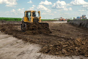 The bulldozer performs excavation work on the construction of the road.
