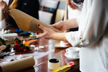 A girl wraps a foam cone in kraft paper for a Christmas craft. Nobilis branches in the background. Close-up of hands. New Year's Eve master class on creating decorations from natural nobilis.