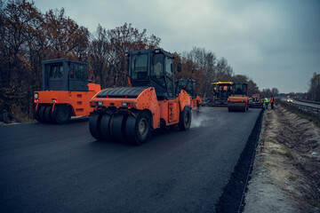 Asphalt rollers rolling new hot asphalt at dusk. Road construction.
