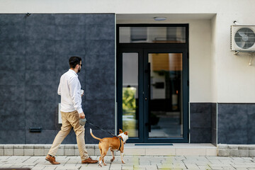 A businessman dressed smart casual entering his building with his dog and returning from a walk....