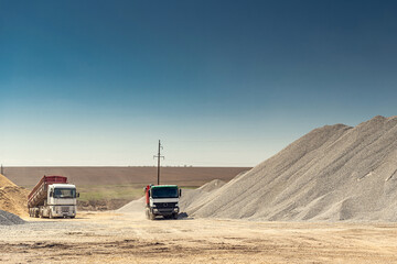 Dump trucks near a pile of rubble in a concrete factory warehouse.