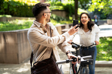 Happy young couple outdoors. Loving couple with bicycle in the park, Handsome man using the phone.