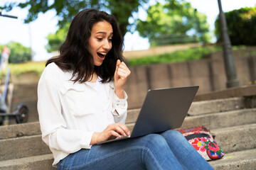 Young businesswoman sitting on steps outdoors and working on laptop. Beautiful girl learning in the park..