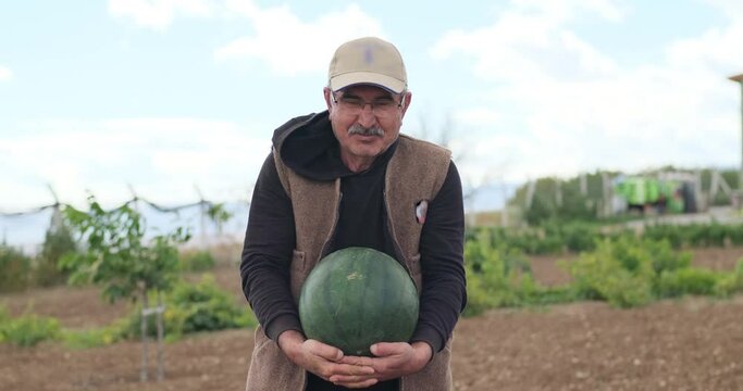 Portrait of a happy smiling farmer in an agricultural field with a ripe watermelon in his hands