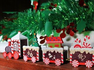 wooden red train on an old stand under a decorated holiday tree, Christmas toys in cute details of home decorations, Christmas style in a festive interior, Christmas toys under a decorated tree