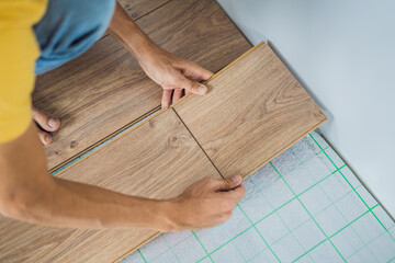 Fototapeta na wymiar Man installing new wooden laminate flooring on a warm film floor. Infrared floor heating system under laminate floor