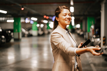 Businesswoman in suit unlocking car on parking. Beautiful woman using the phone